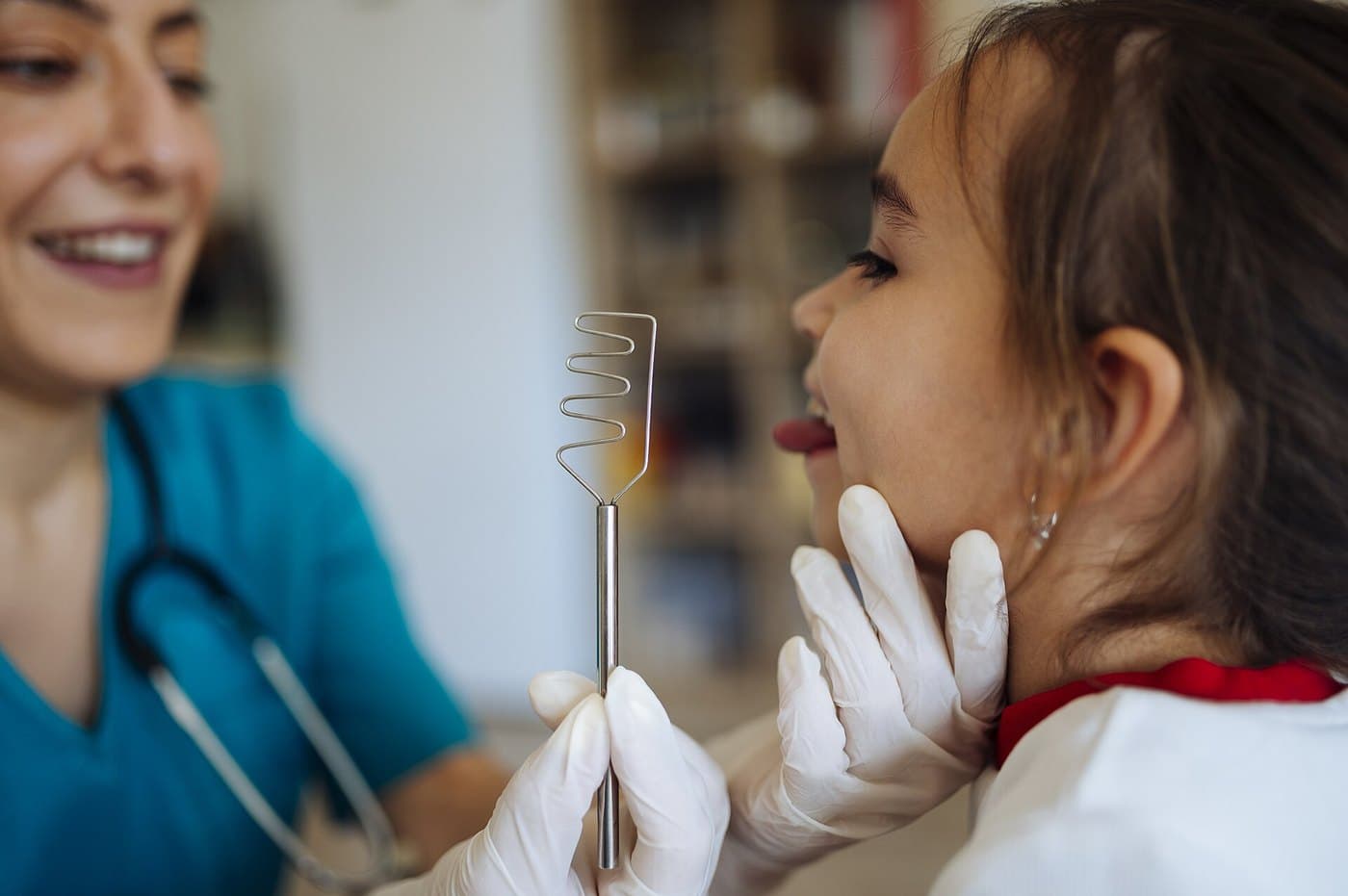 Orvos nyelvlapoccal vizsgálja egy kislány torkát egy világos rendelőben