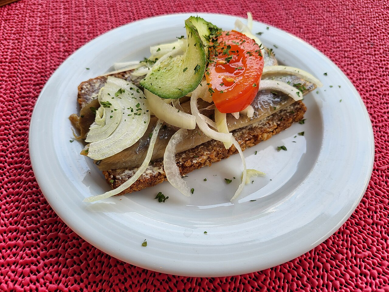 Heringfilé vöröshagyma-karikákkal teljes kiőrlésű rozskenyéren, paradicsom- és uborkaszelettel