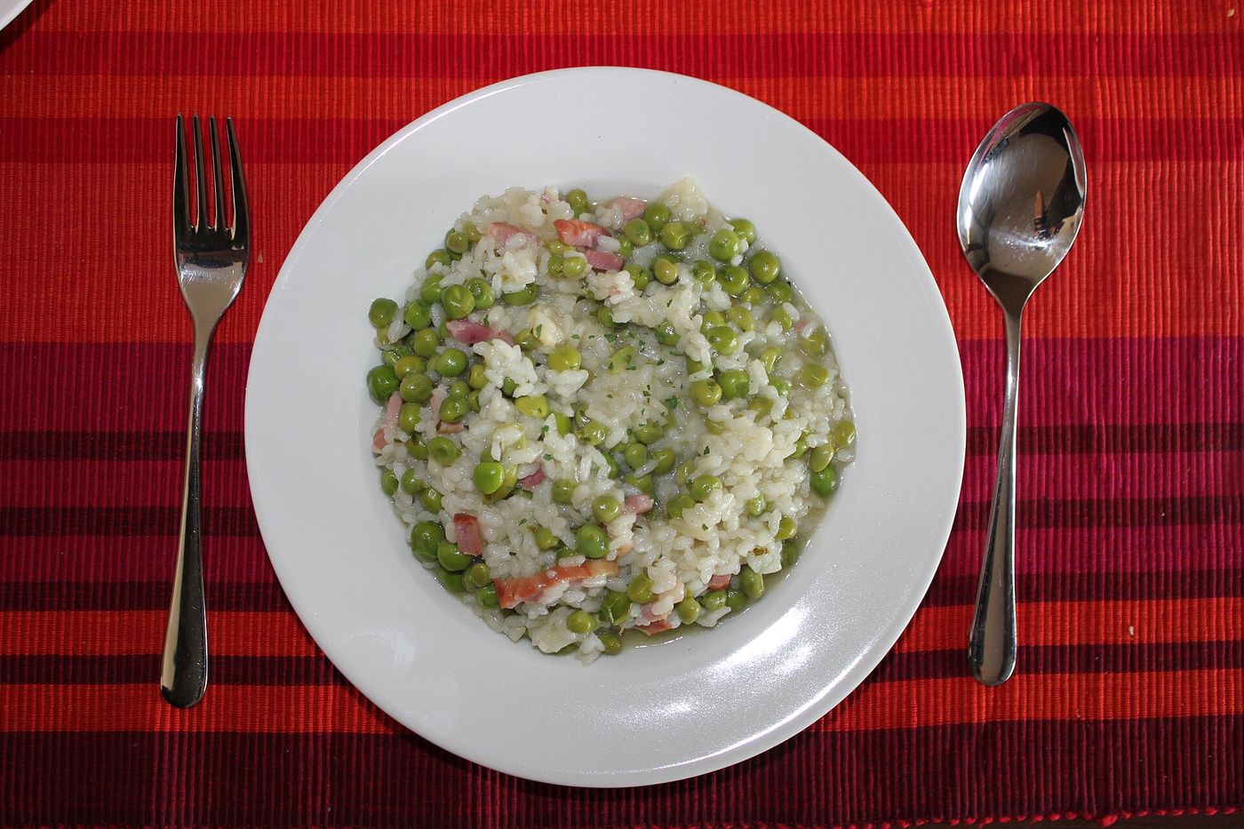 Krémes zöldborsós rizottó sonkakockákkal és reszelt parmezánnal, fehér tányéron, felülnézetből